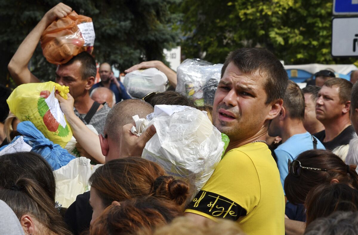 Residentes locales, muchos de los cuales huyeron de la guerra, se reúnen para entregar donativos como medicamentos, ropa y pertenencias personales a sus familiares en los territorios ocupados por Rusia, el domingo 14 de agosto de 2022, en Zaporiyia, Ucrania. (AP Foto/Andriy Andriyenko)