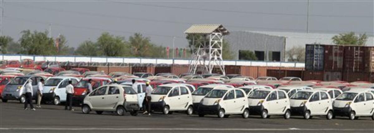 People walk past Nano,Tata's ultra cheap micro car, parked at a new factory at Sanand, about 40 kilometers (25 miles) from Ahmadabad, India, Tuesday, June 1, 2010. Tata Motors plans to start commercial production of the Nano in Gujarat state next week. So far, the company has delivered 30,763 Nanos. It also reported higher-than-expected consolidated annual profits of $549.7 million Thursday thanks to a turnaround in its Jaguar Land Rover business, stoking the global ambitions of India's largest vehicle maker despite uncertainties from Europe's debt crisis. (AP Photo/Ajit Solanki)