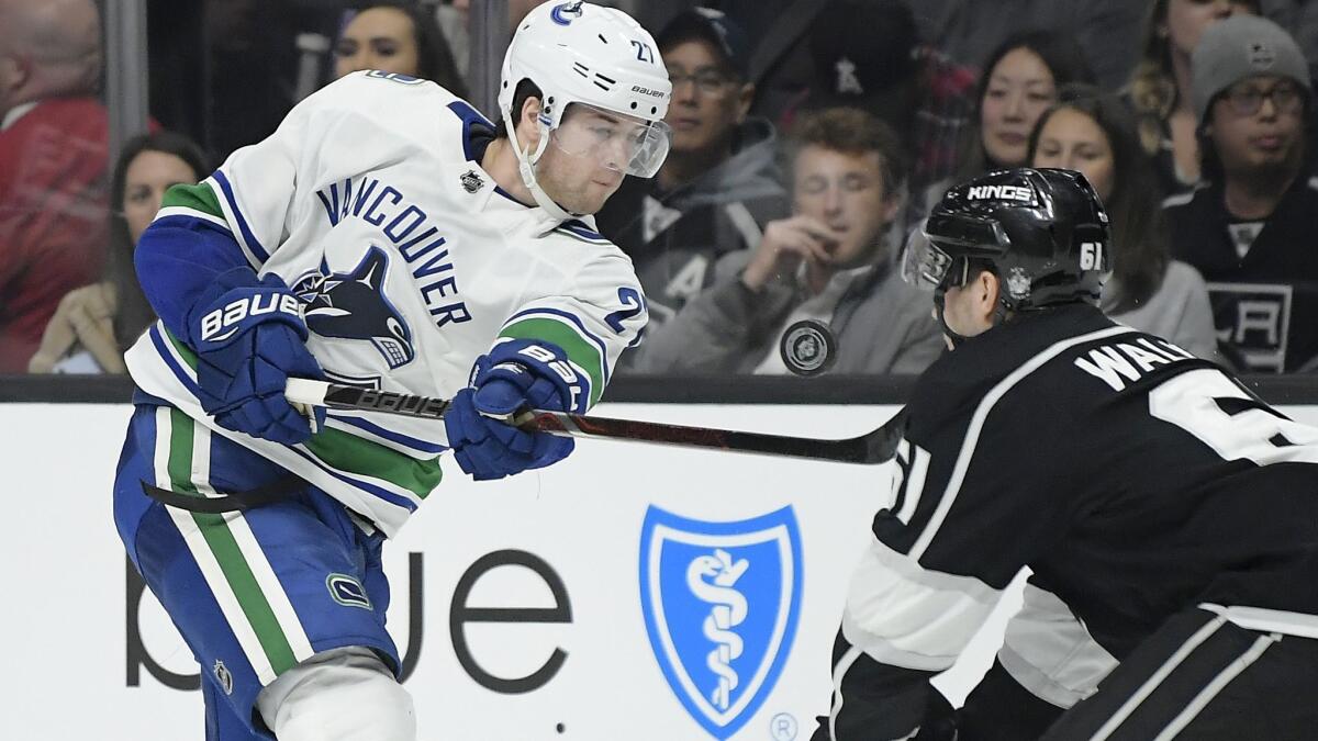 Vancouver Canucks defenseman Ben Hutton, left, shoots the puck into the face of Kings defenseman Sean Walker during the third period on Thursday. Walker left the game bleeding from the mouth.