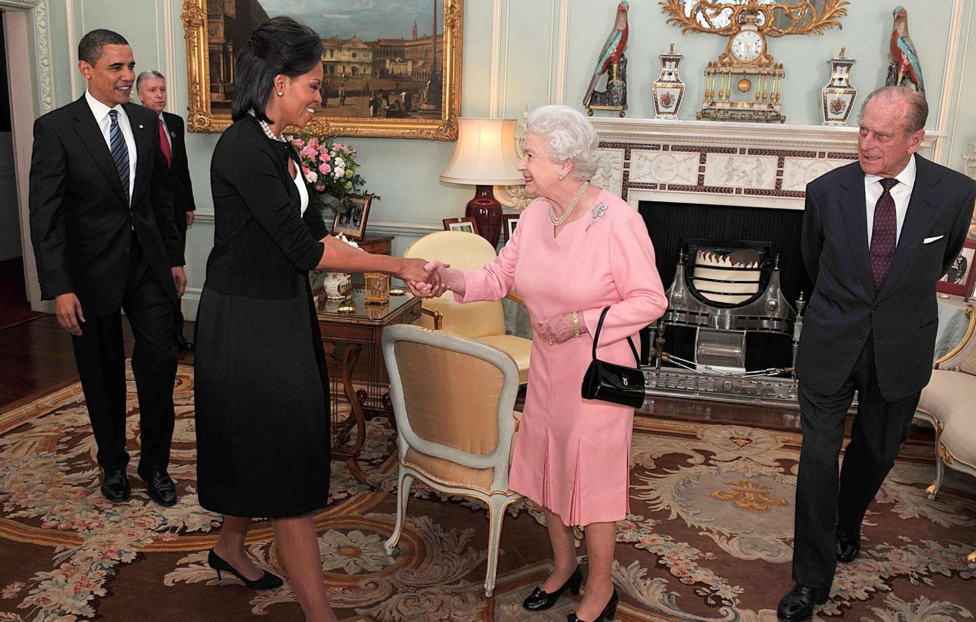 Queen Elizabeth II clasps hands with First Lady Michelle Obama, flanked by Prince Philip and President Obama
