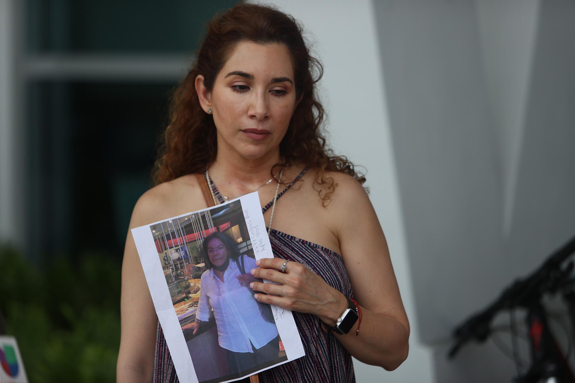 Standing outside the building, a woman holds a picture of another woman.