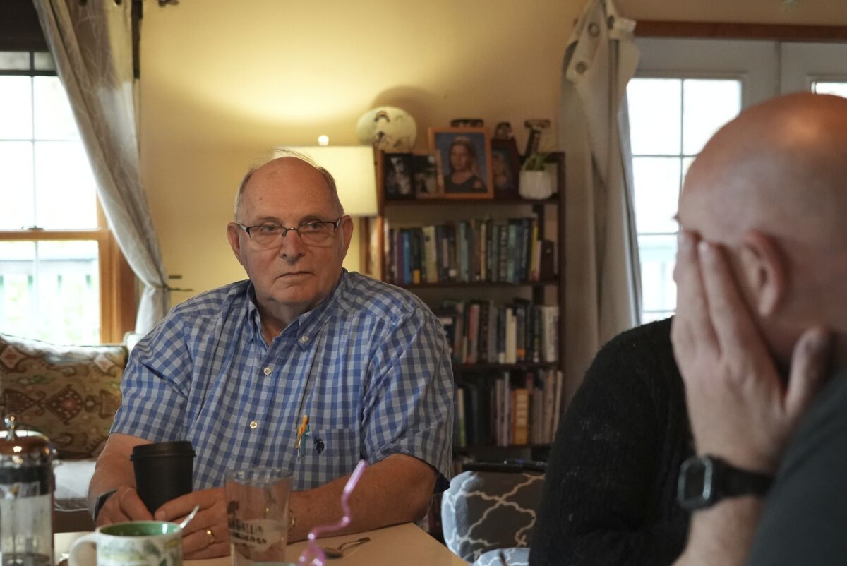 Two men sit at a table in a home. 