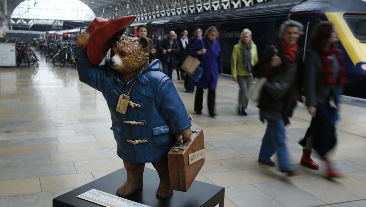 Commuters alighting from a train pass by a statue of Paddington Bear on the platform at Paddington railway station in London.