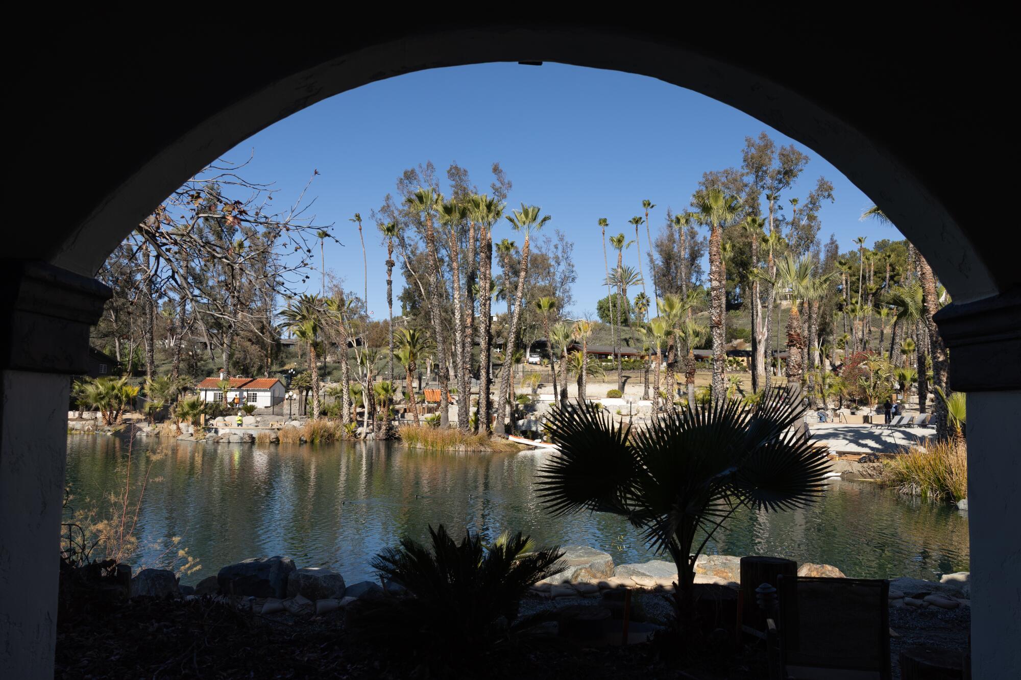 A view through an arch onto a pool of water surrounded by trees, under a blue sky