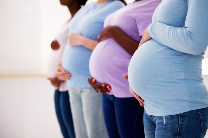 Pregnant women stand in a row, holding their bellies.