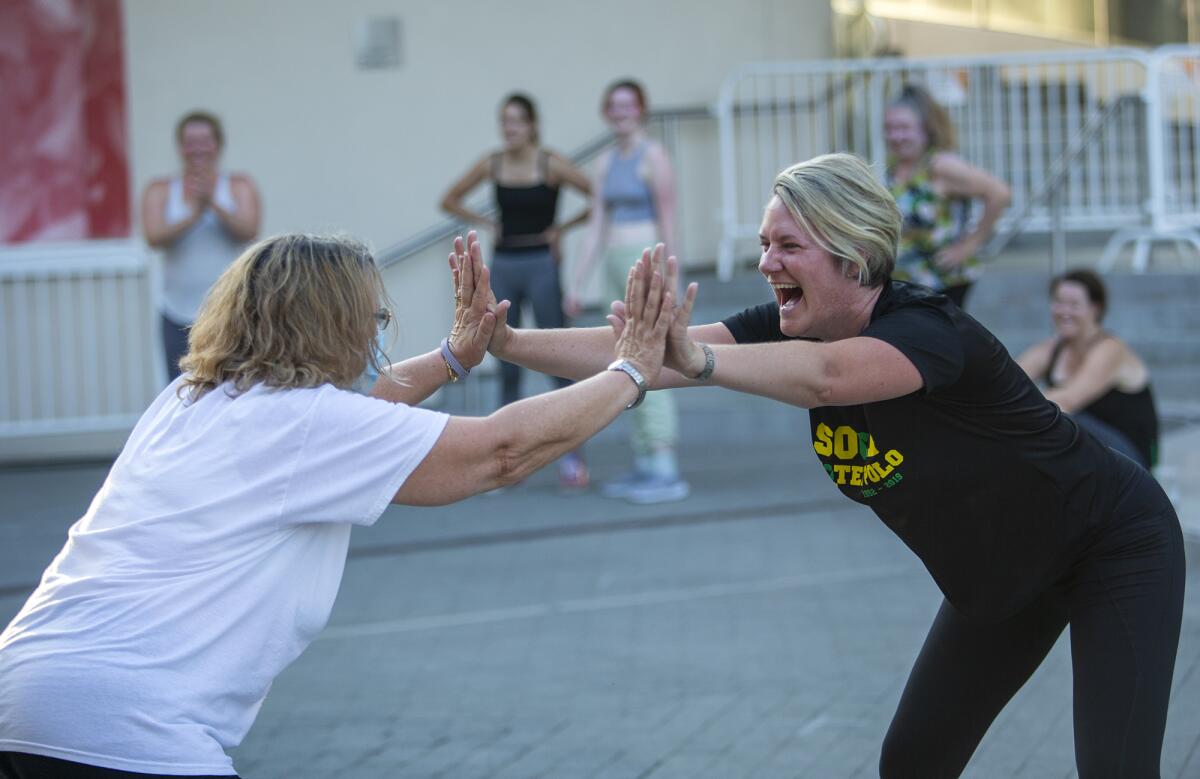 Chris Upham, left, and Sarah Scott high five during a capoeira class at Segerstrom Center's Argyros Plaza on Tuesday.