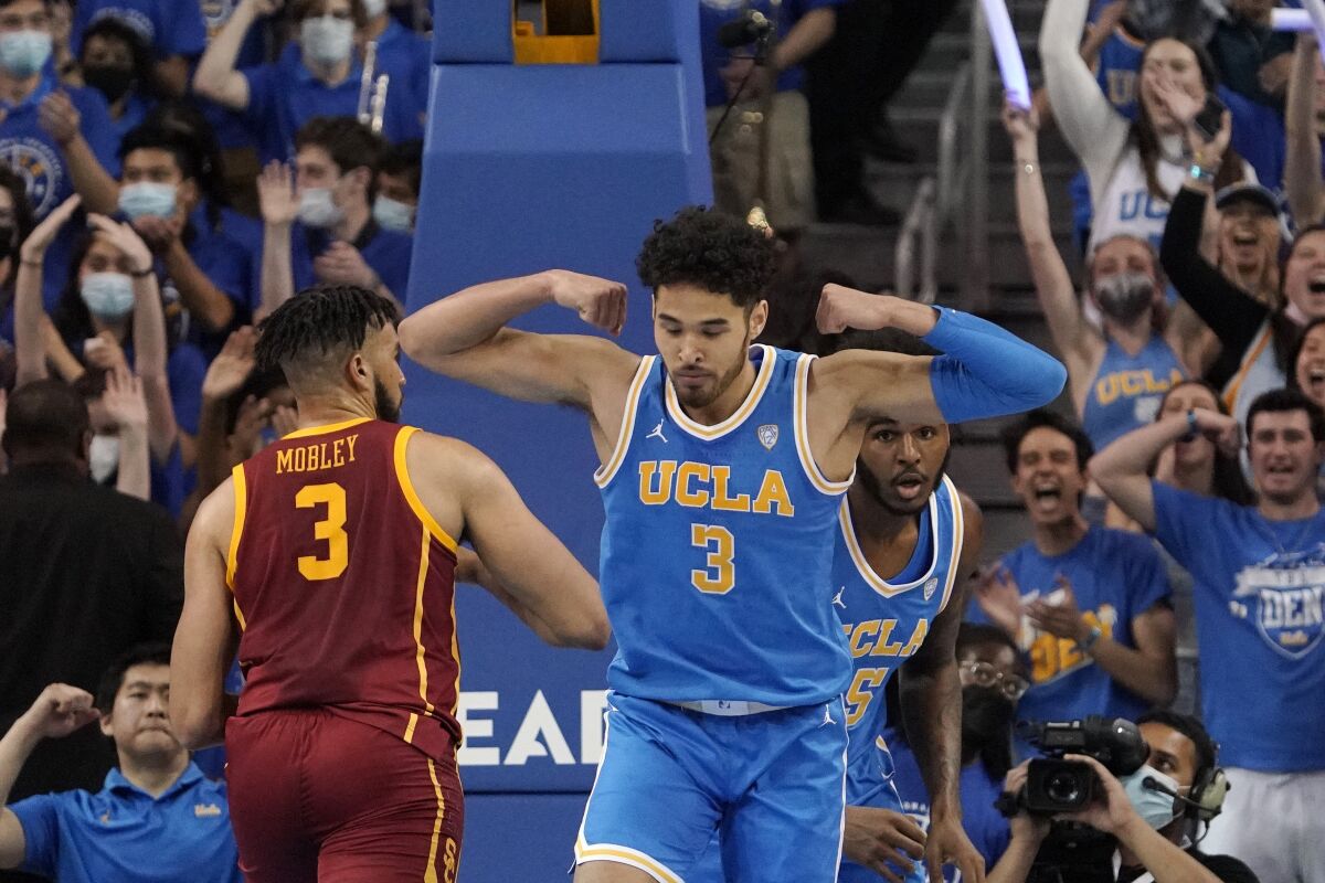 UCLA guard Johnny Juzang celebrates by flexing after scoring in front of USC forward Isaiah Mobley.