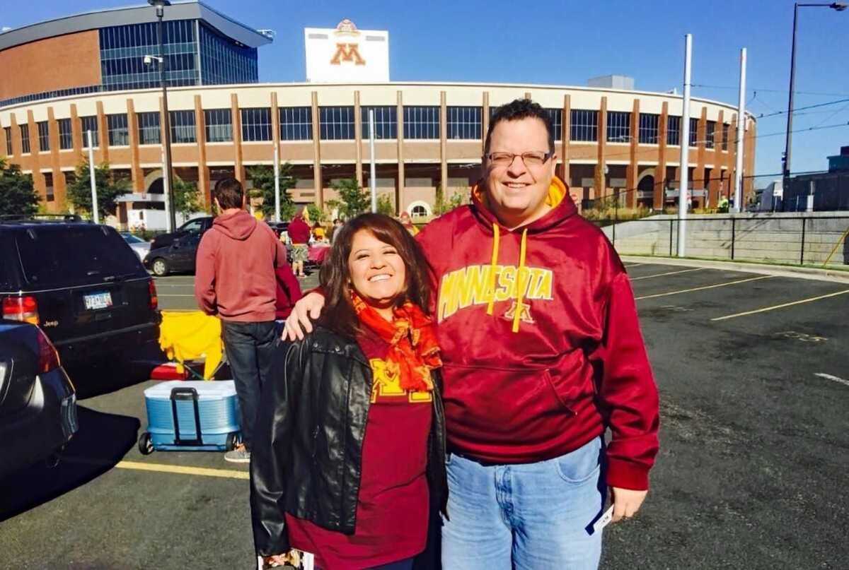 Greg Flugaur stands outside a stadium with his arm around his wife, Mireya Hernandez, 
