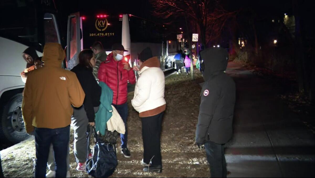 People in winter coats stand outside a bus at night.