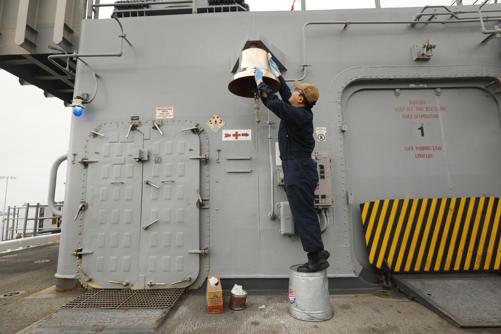 On board the amphibious assault ship USS Essex, Petty Officer 3rd class Isaac Schweitzer shines the ship's bell