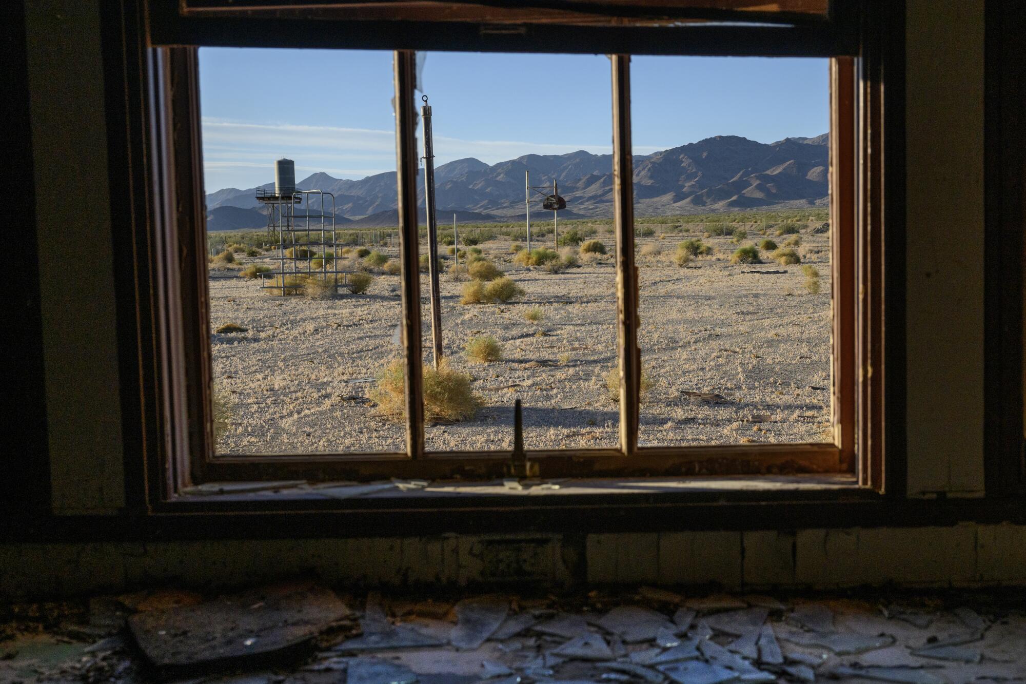 Playground equipment and tumbleweeds are seen through a broken window.