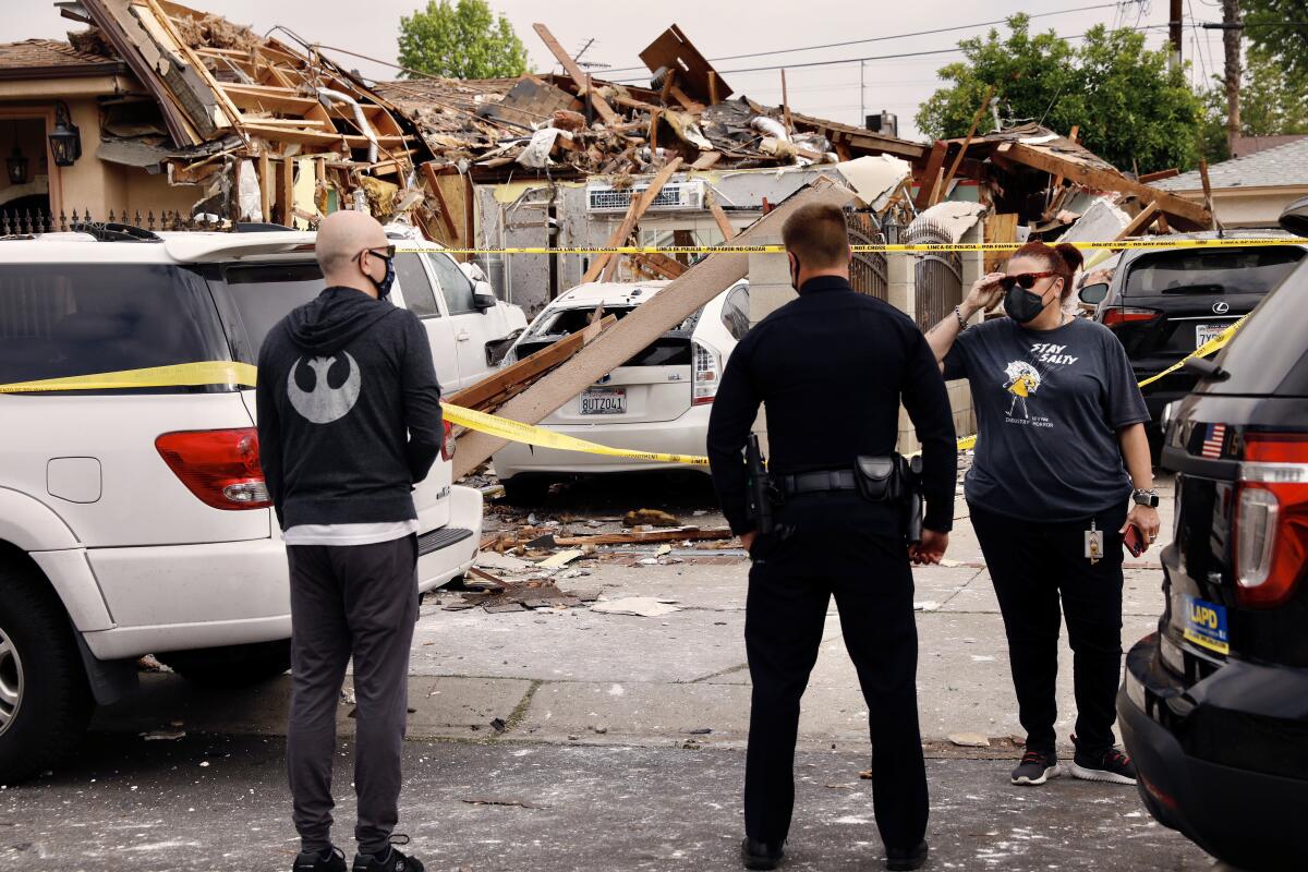 Two people speak to a police officer in front of a destroyed garage
