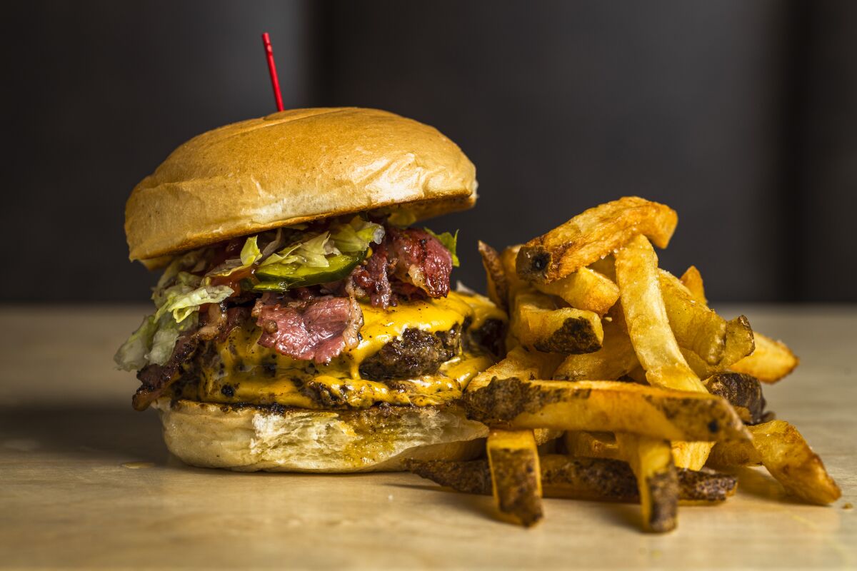 A photo of a pastrami HiHo Cheeseburger with a side of fries.