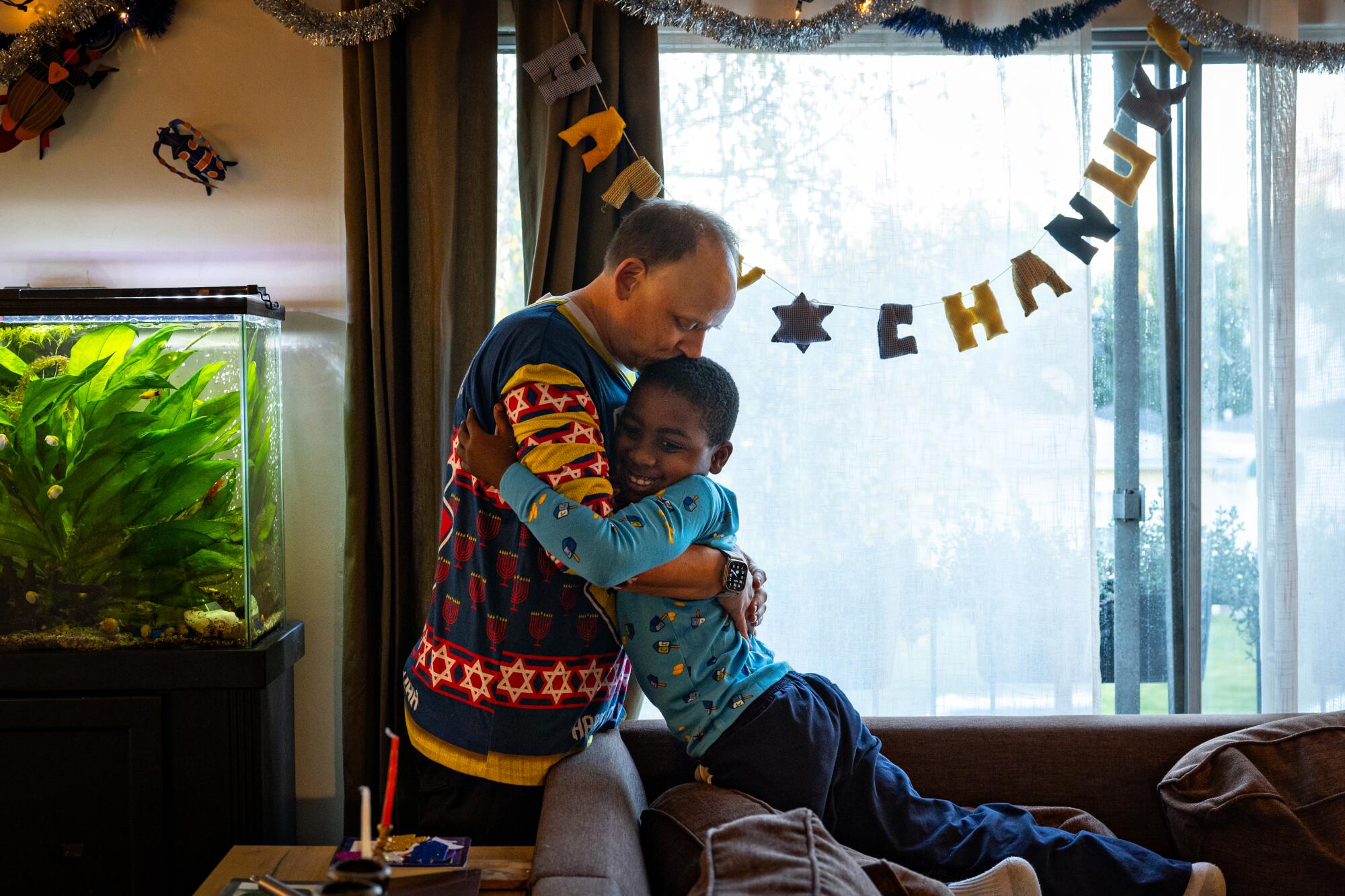 A man and boy embrace as a Happy Chanukah sign stretches across a window behind them.
