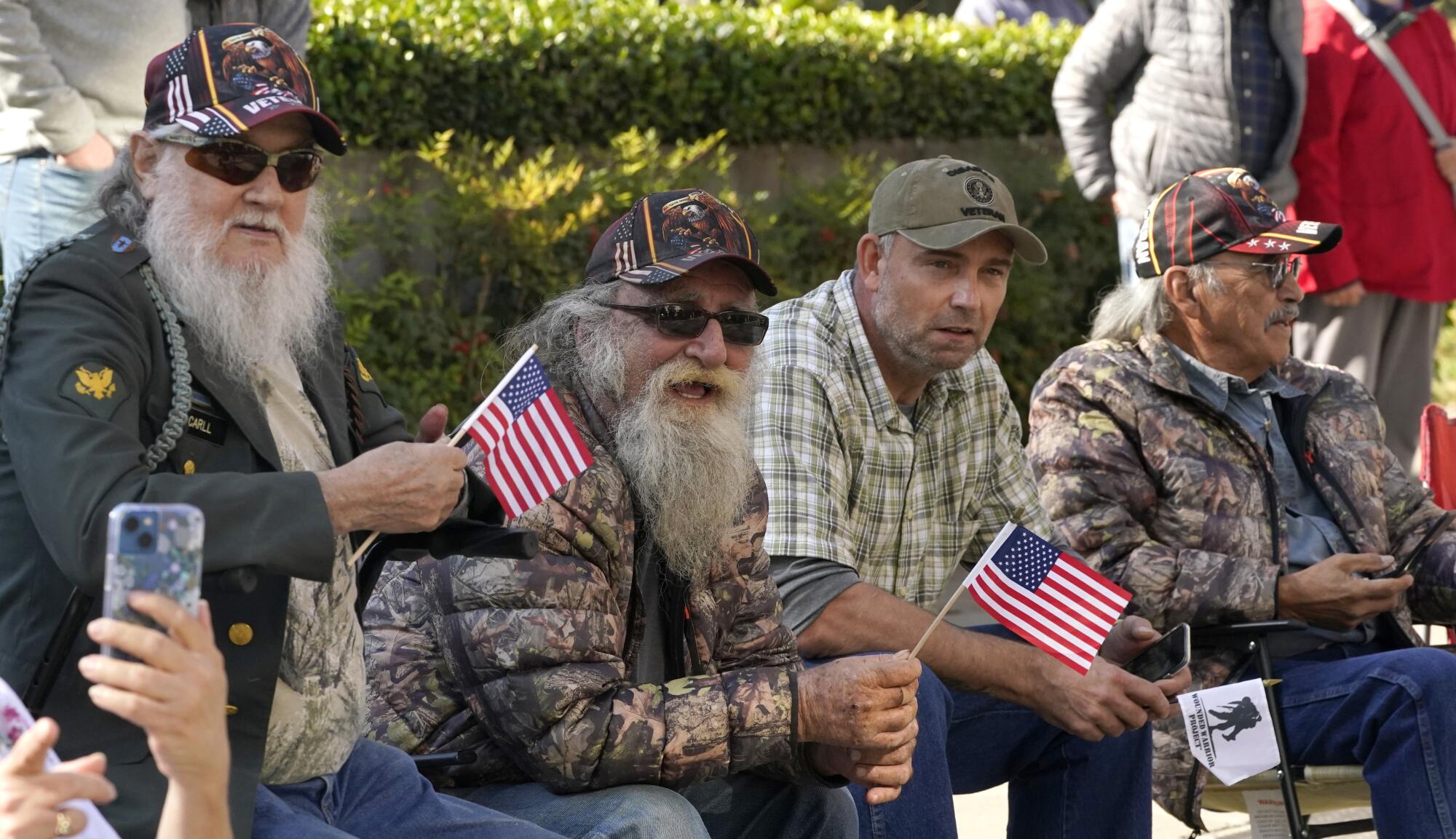 Four men sit on a bench watching a parade