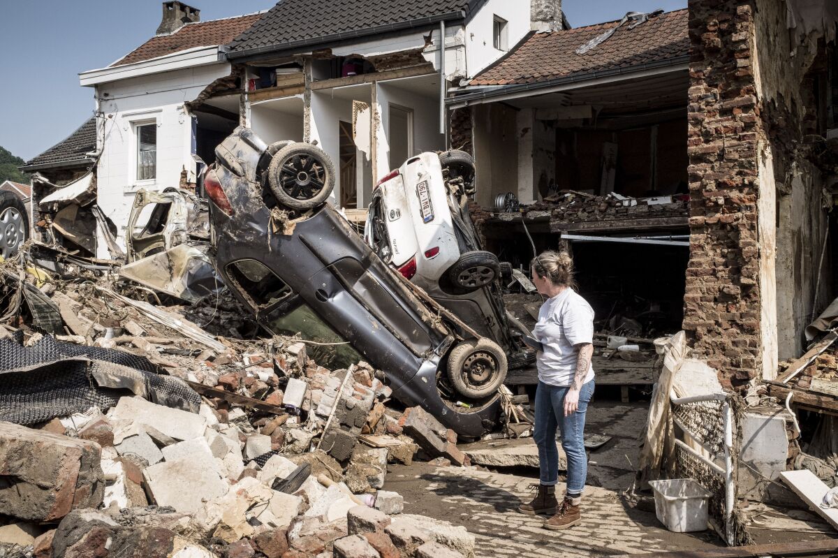 FILE - In this file photo dated Monday, July 19, 2021, a woman looks at cars and homes damaged after torrential rain caused flooding in Liege, Belgium. A new massive United Nations science report is scheduled for release Monday Aug. 9, 2021, reporting on the impact of global warming due to humans. (AP Photo/Valentin Bianchi, FILE)