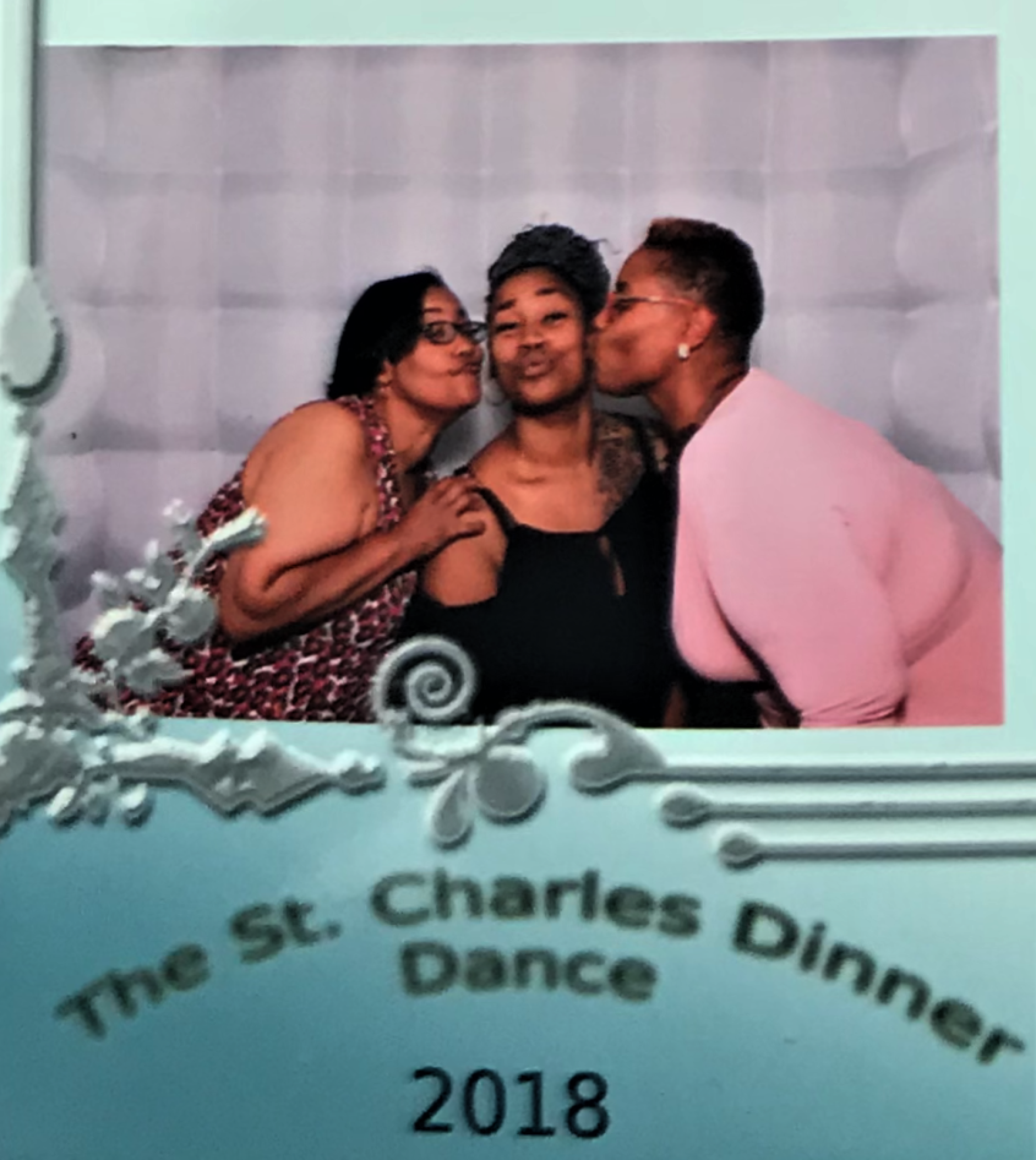 A woman, flanked by two others, blows a kiss. A sign below says The St. Charles Dinner Dance 2018