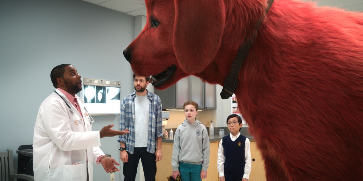 A giant red dog towers over a veterinarian as a man and two children look on in the movie “Clifford the Big Red Dog.” 