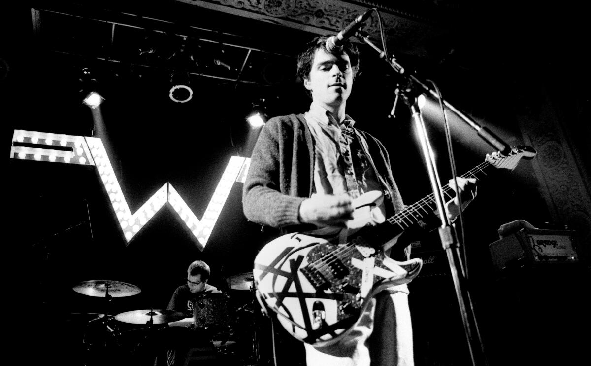Weezer members play instruments on a dark stage.