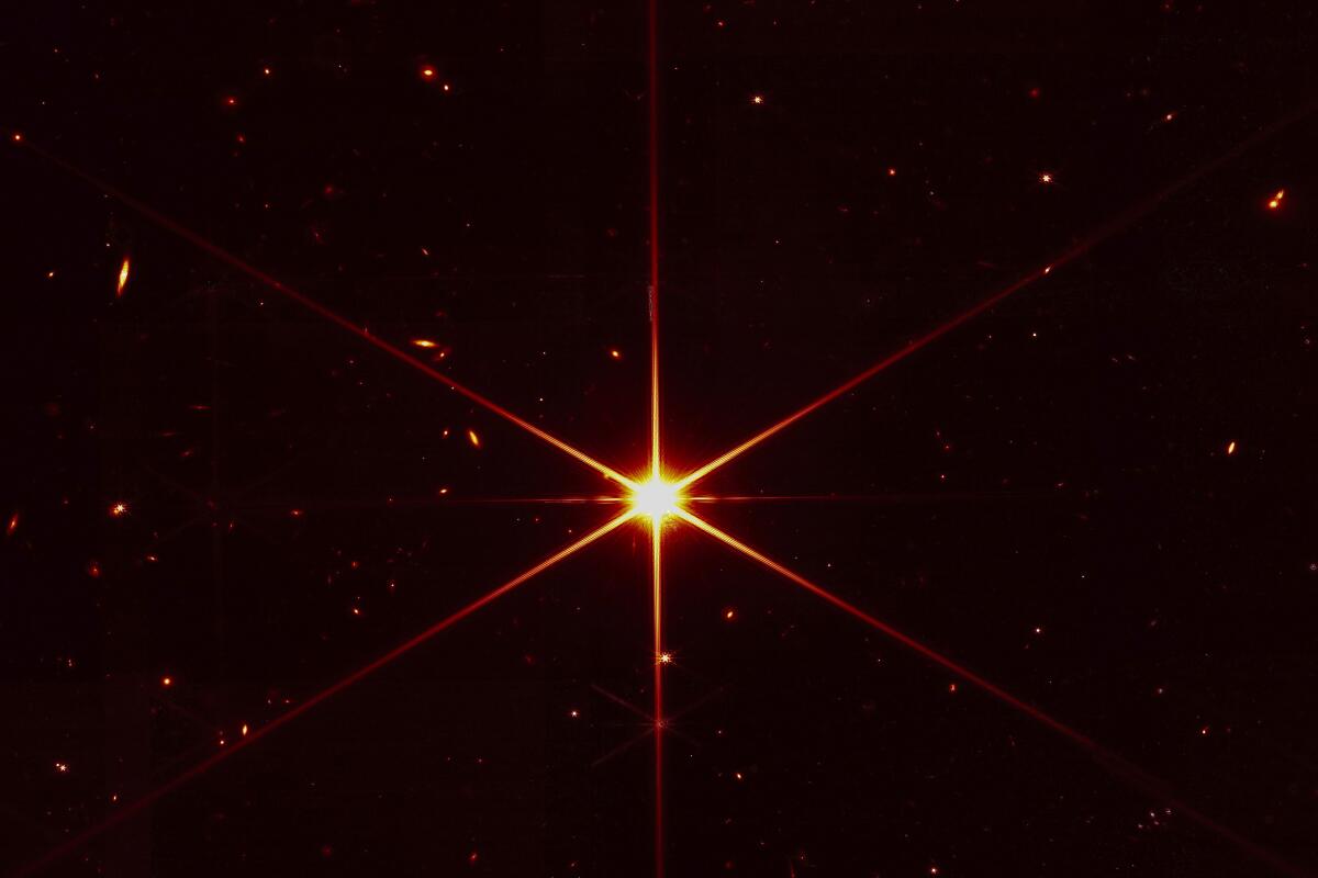 A star shines brightly in space, surrounded by dimmer stars and galaxies