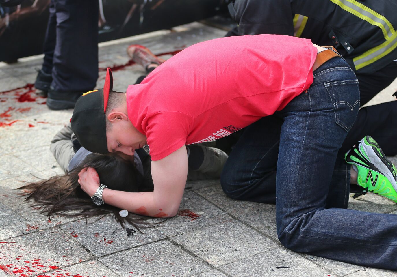 A man comforts an injured woman on the sidewalk after the first explosion.