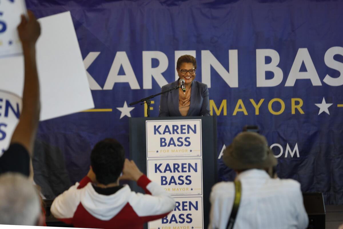 Karen Bass speaks into a microphone at a lectern in front of a crowd of supporters.