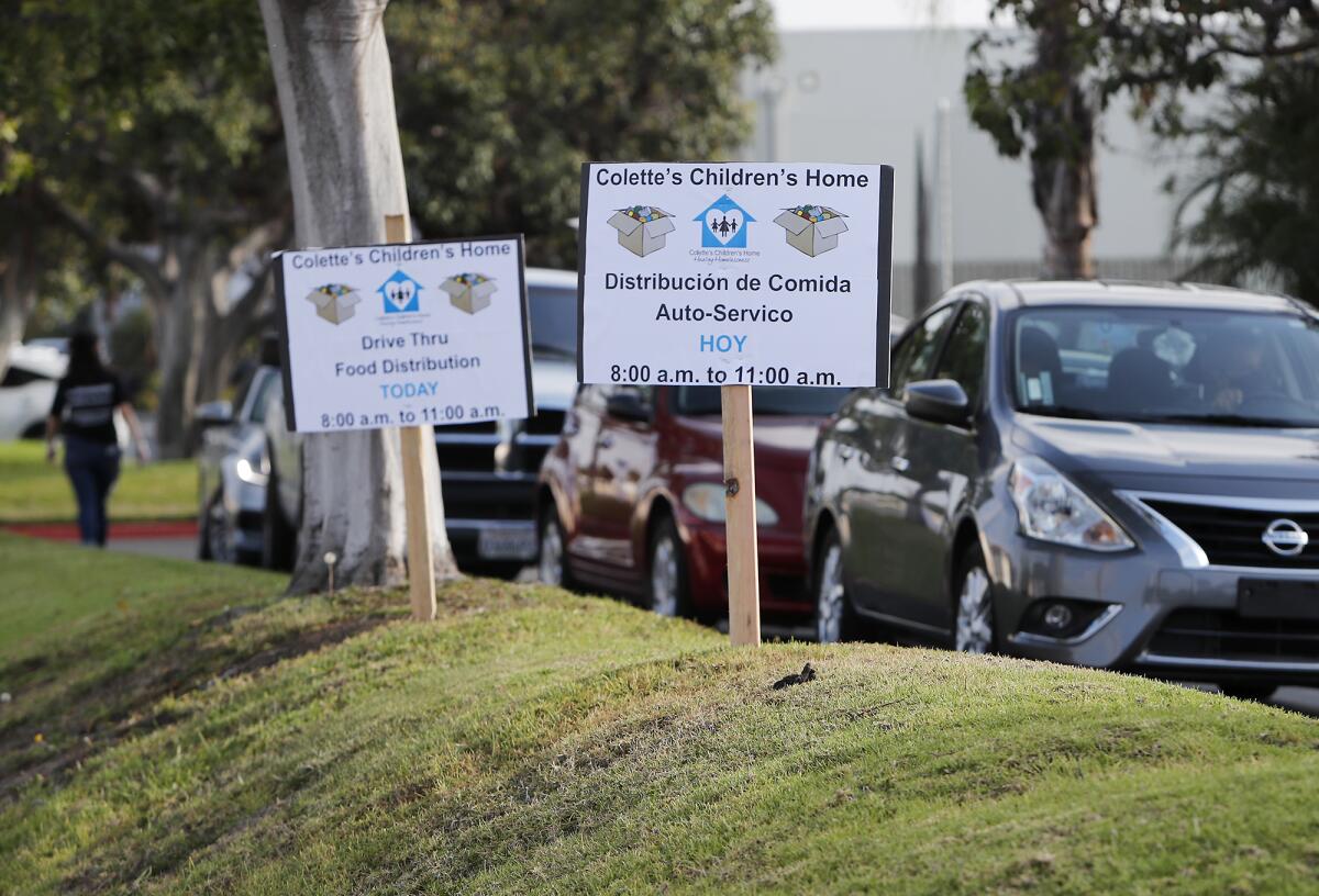 Spanish and English signs posted along Gothard Street notify drivers of Colette's Children's Home drive-through food distribution on Saturday morning in Huntington Beach.