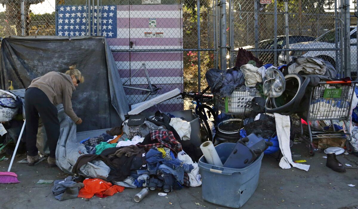 FILE - A woman camping in downtown San Diego sorts through her belongings on a sidewalk that was being sprayed with a bleach solution to fight a deadly hepatitis A outbreak on Sept. 25, 2017. Homeless residents of downtown San Diego encampments will be paid to pick up trash in their neighborhood as part of a new pilot program. The program was launched by retired attorney Brian Trotier, who for years has been handing out food to people in need as a volunteer with a local nonprofit, the San Diego Union Tribune reported Sunday, March 13, 2022. (AP Photo/Gregory Bull, File)