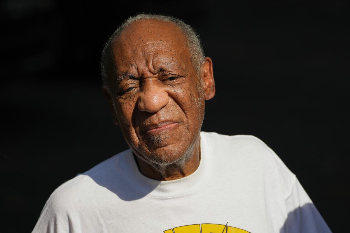 Bill Cosby grimaces in the sun while clad in a white T-shirt with a design on it