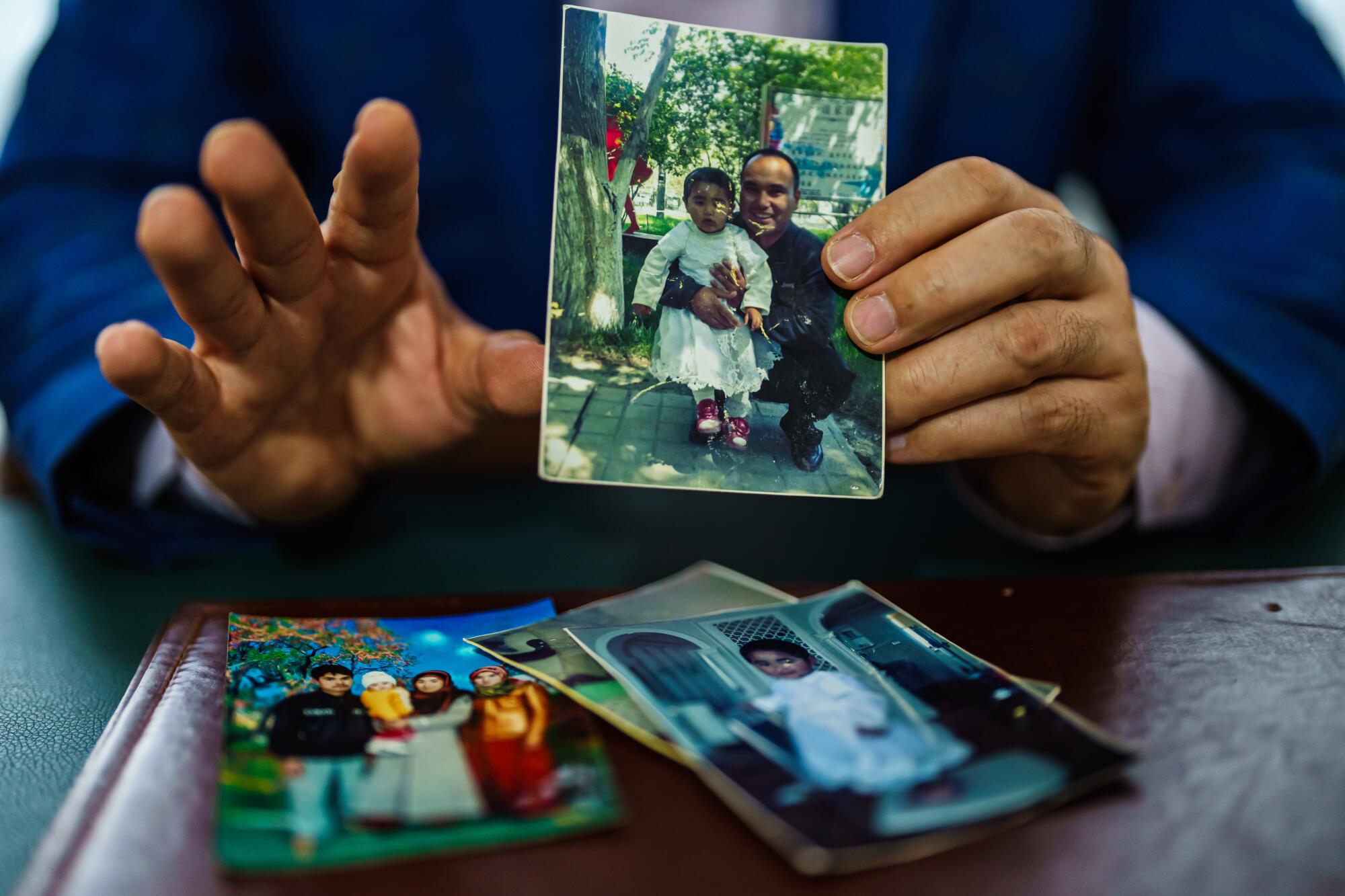 A closeup of a man's hands; he's holding a photo of a man and child. Other photos lie on a table.