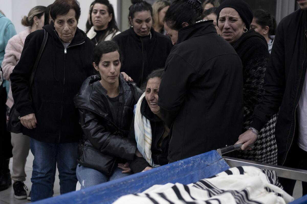 A sobbing woman is comforted among mourners gathered around a body  covered with a shroud