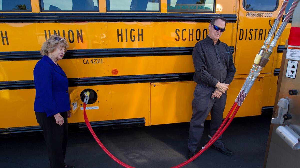 Jeff Hutchings, manager of maintenance and operations for the Huntington Beach Union High School District, watches as school board President Bonnie Castrey fills a bus with compressed natural gas Monday at the district's new CNG station.