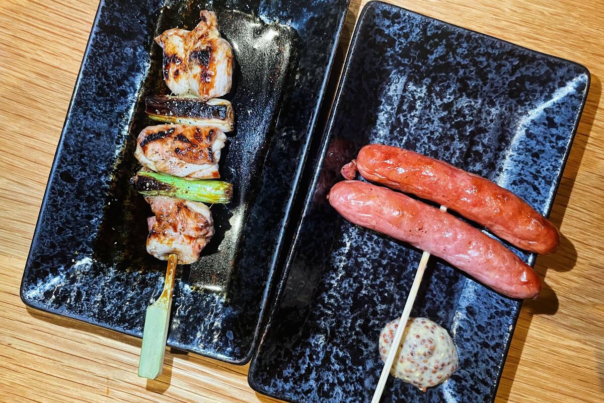 An overhead photo of negitama (chicken and onion) and sausage skewers on two rectangular black plates