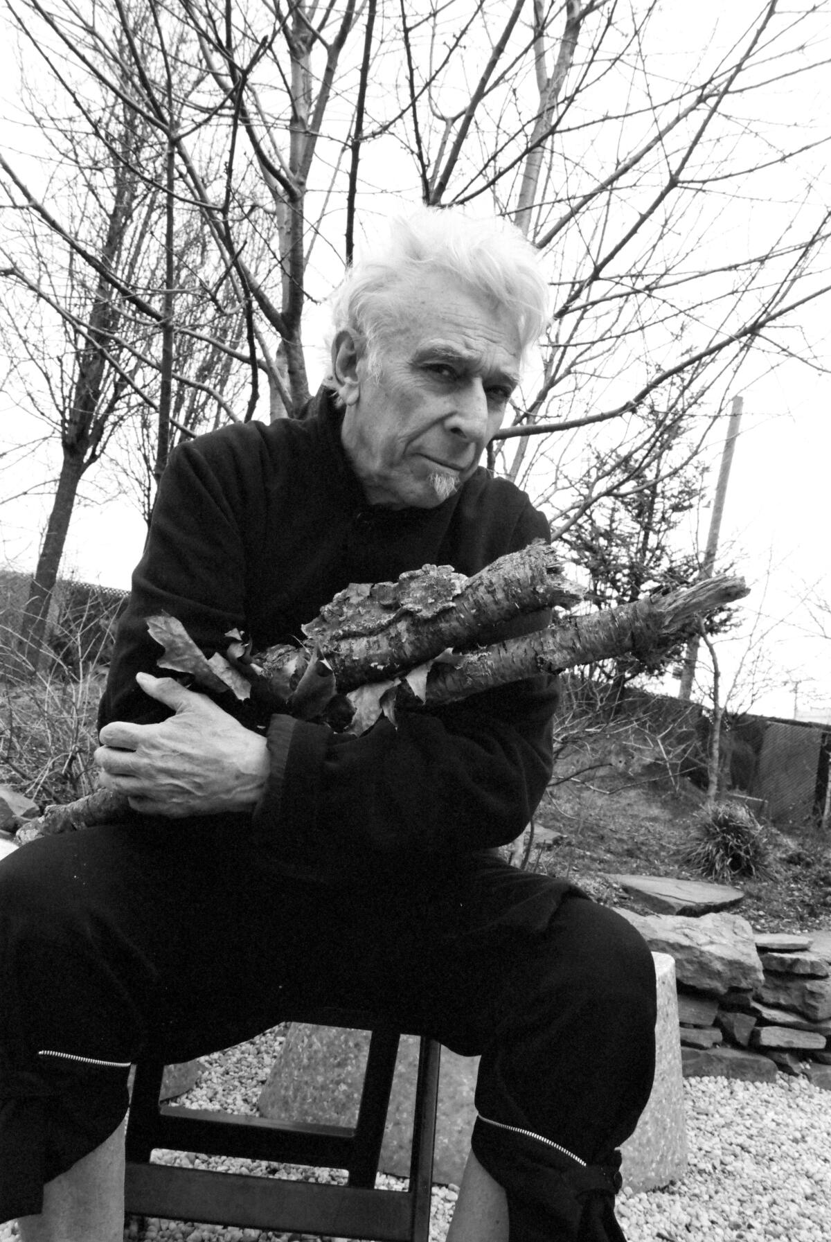 An older man sits outside holding firewood