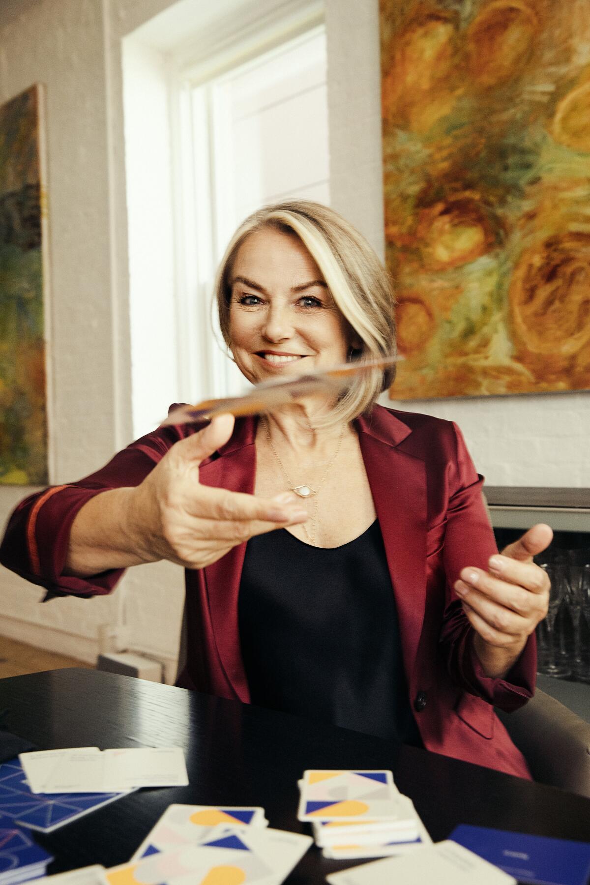 A woman at a dining table throws cards at the camera