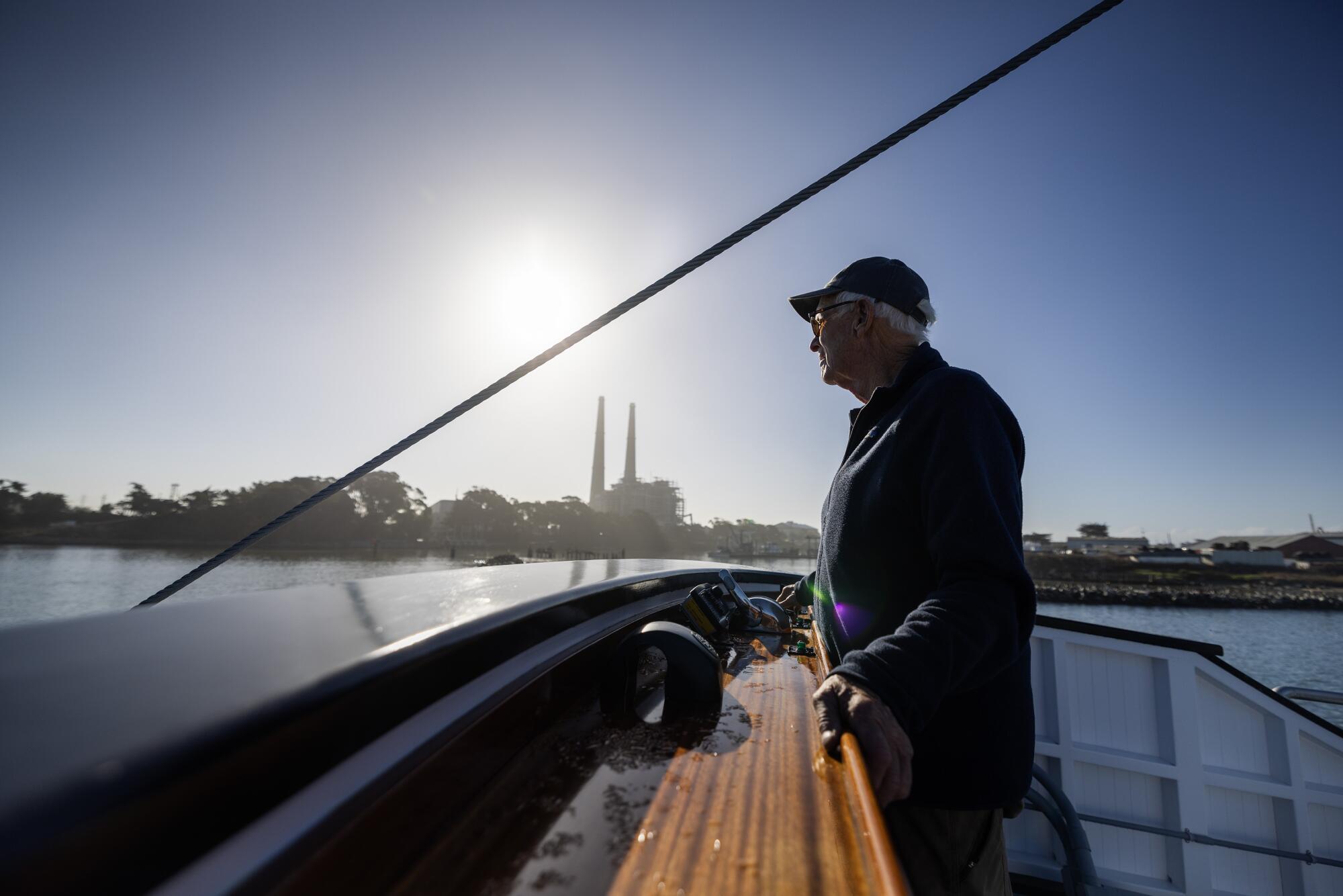 A man stands aboard a boat backlit by a low sun. 