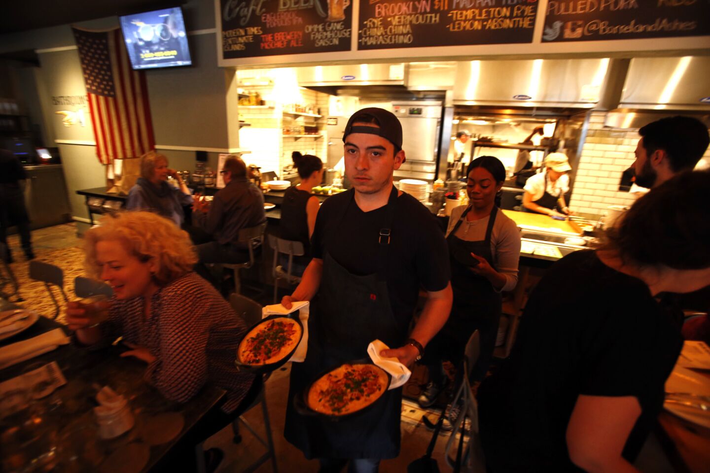 Expediter Gilbert Castillo delivers a couple of plates of food at Barrel & Ashes.