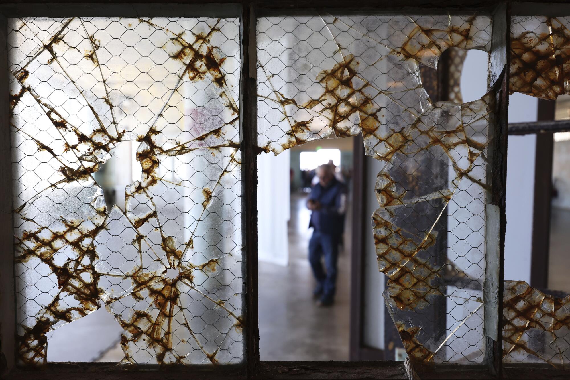 A visitor is framed by broken glass while touring Alcatraz Island.