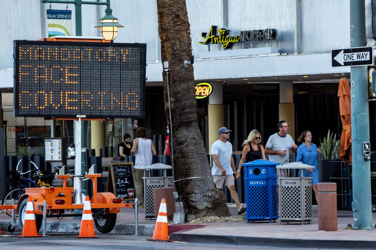 Pedestrians walk past a sign reminding them to wear a face covering in downtown Palm Springs on July 16.