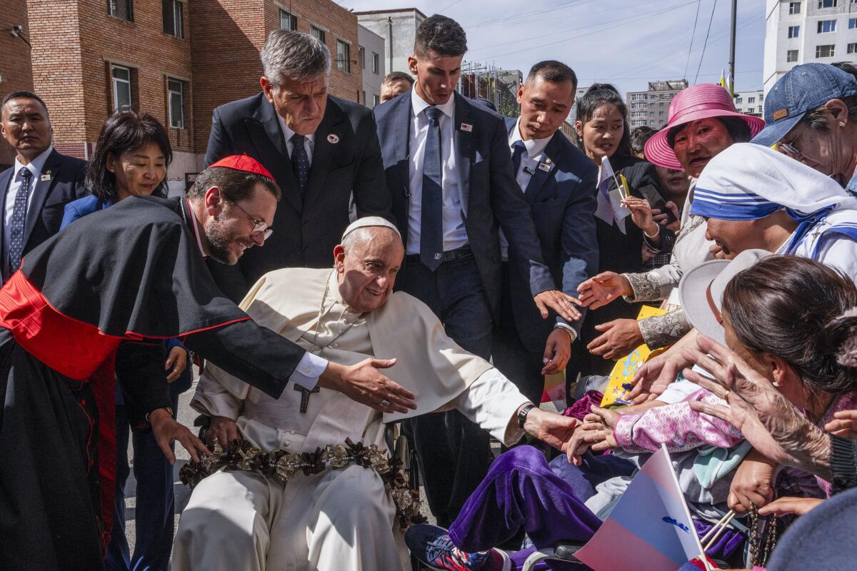Pope Francis sits while greeted by a cardinal and others in Ulan Bator, Mongolia