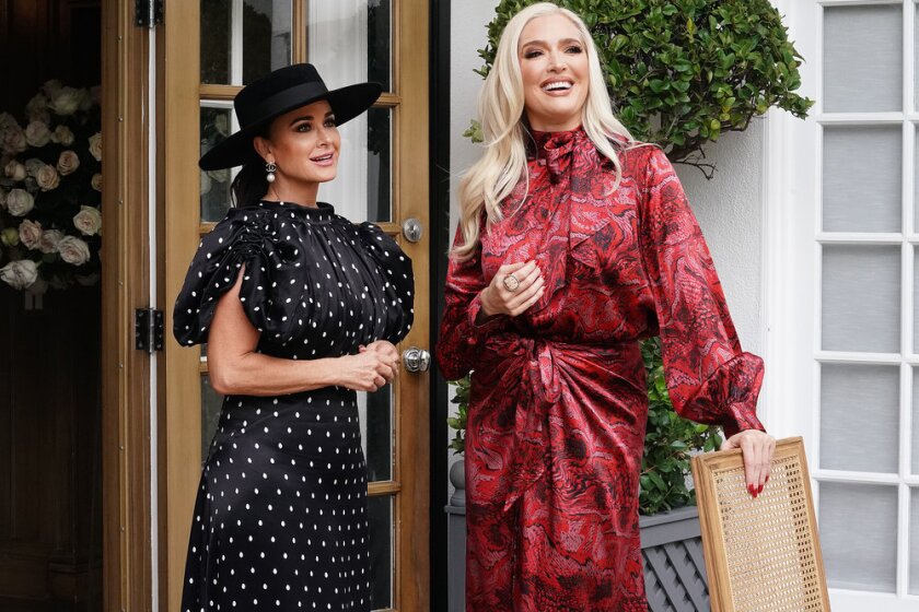 A woman in a black-and-white dress and hat standing next to a woman in a maroon dress