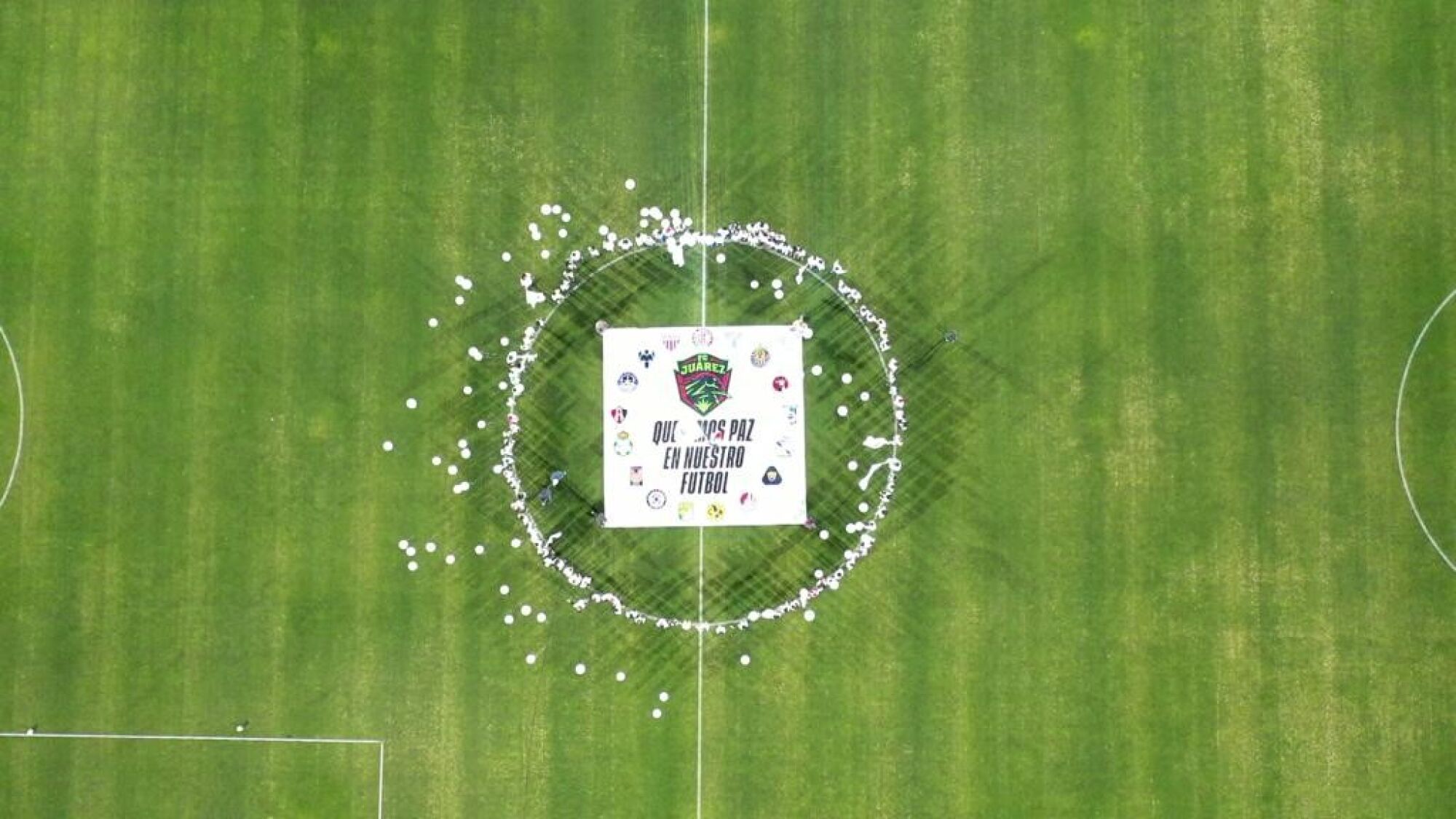Children gather in the middle of a soccer field and hold a sign that calls for peace