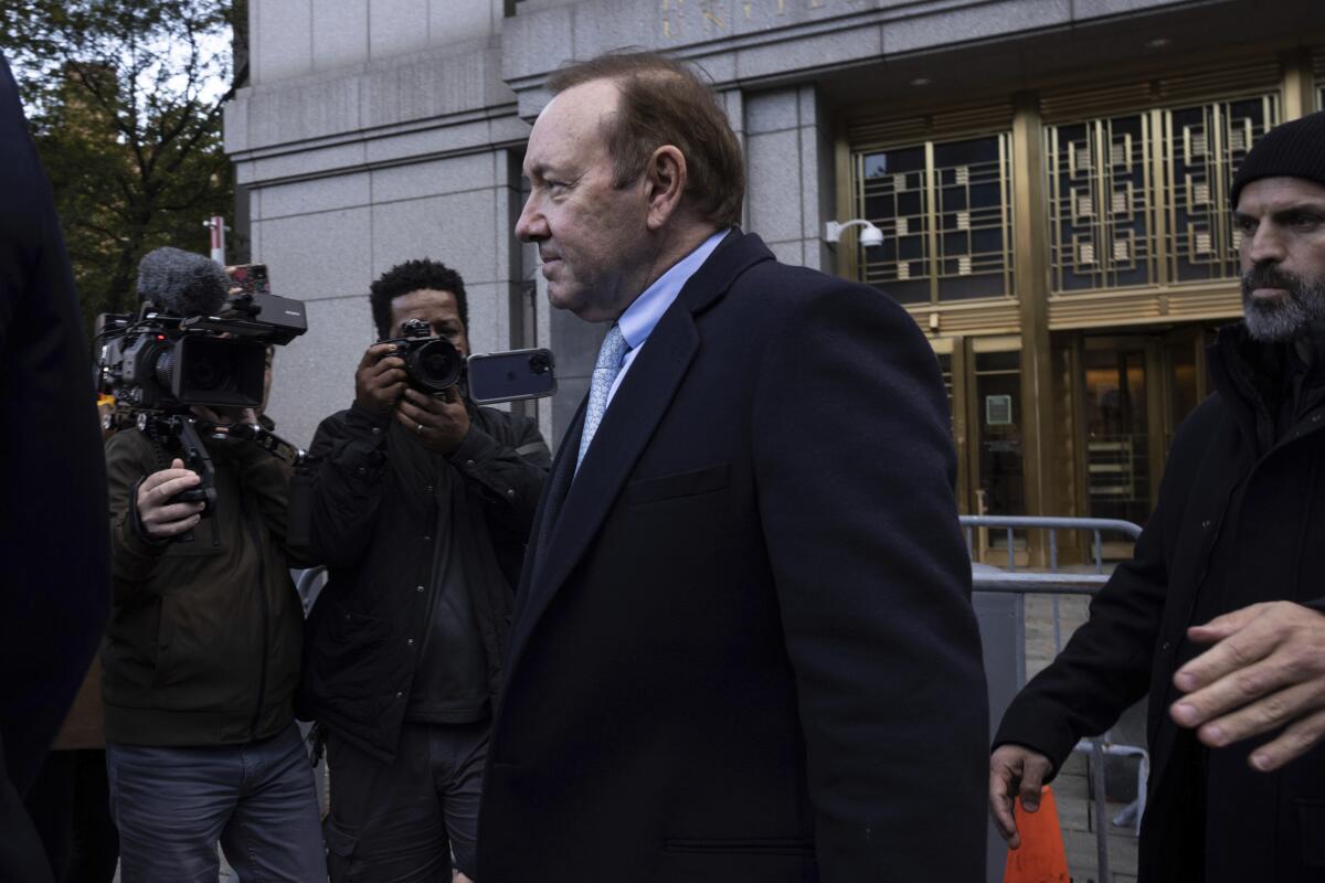 A man in a dark suit leaves a courthouse while surrounded by photographers.