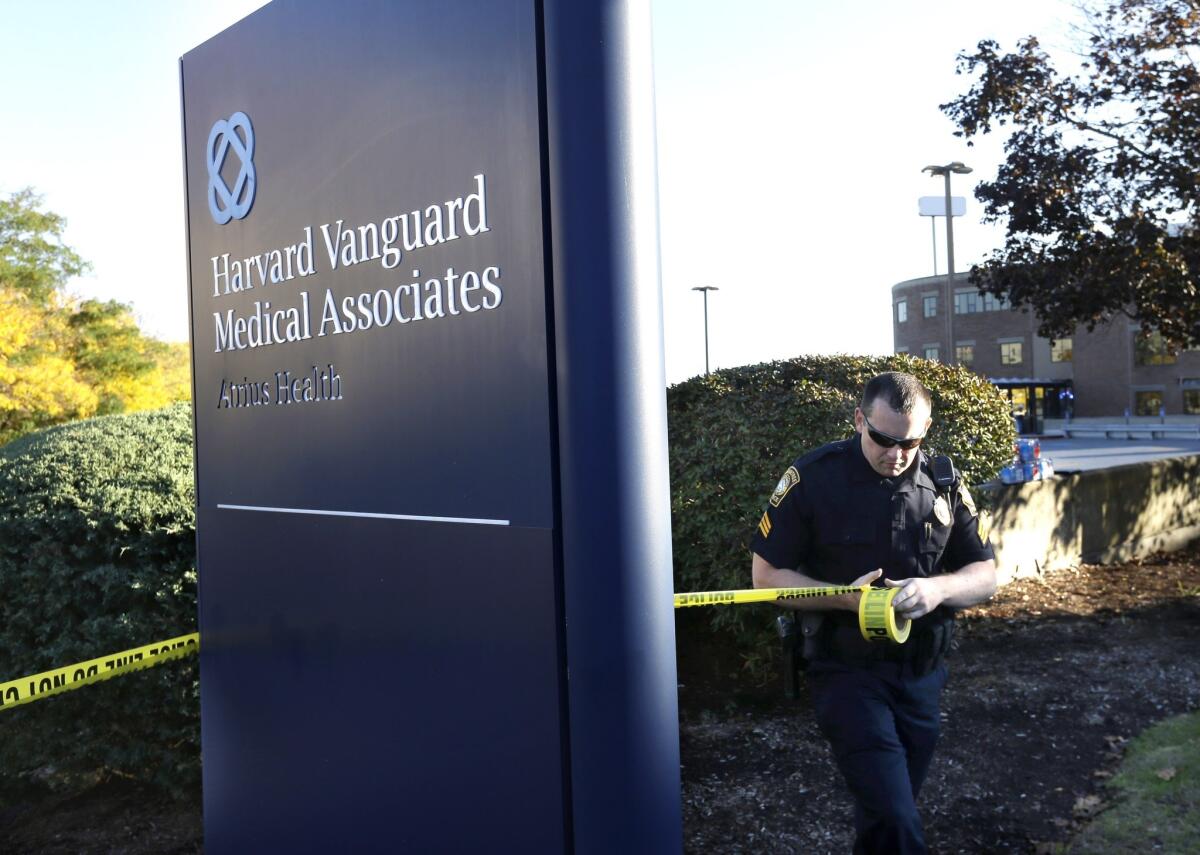 A law enforcement official places police tape around a sign to the Harvard Vanguard Medical Associates on Sunday, Oct. 12, 2014, in Braintree, Mass.