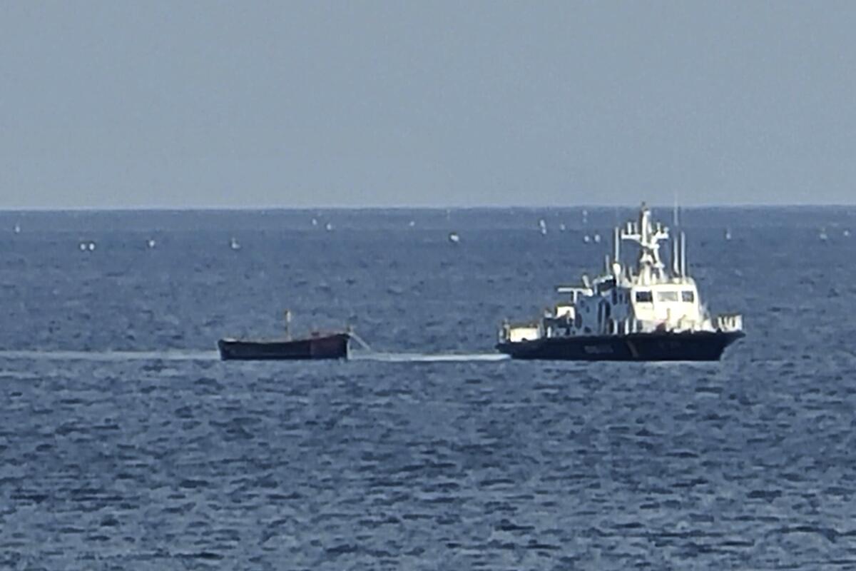 A small wooden boat being towed by a larger ship