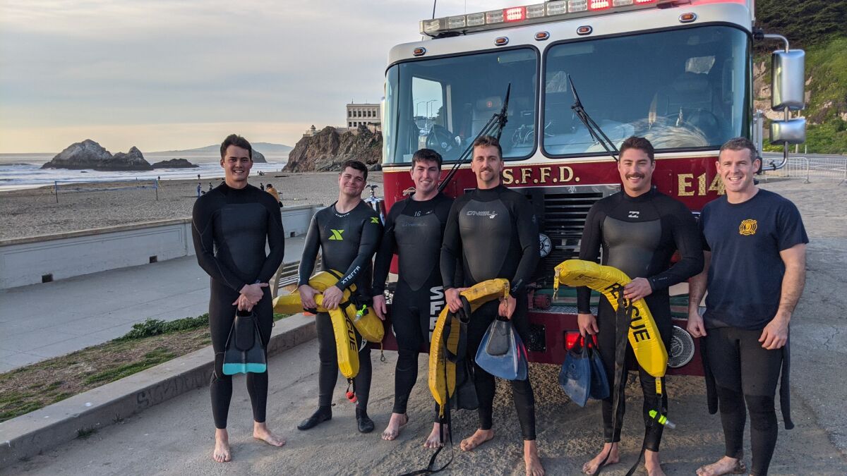 Fire department rescue swimmers in wet suits stand near beach.