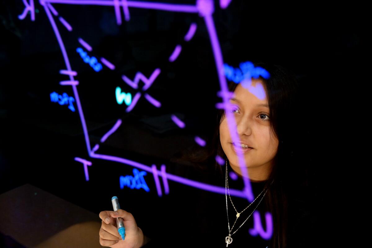 A high school girl works on a geometry problem on a board.