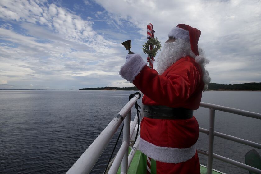 Jorge Barroso, dressed as Santa Claus, waves from a boat as he arrives to distribute gifts to children in the riverside communities of Manaus, Amazonas state, Brazil, Saturday, Dec. 17, 2022. (AP Photo/Edmar Barros)