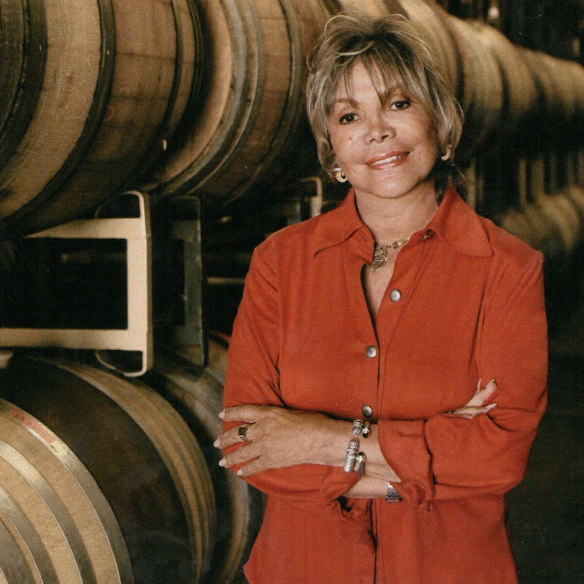 a woman standing in front of wine barrels with her arms crossed