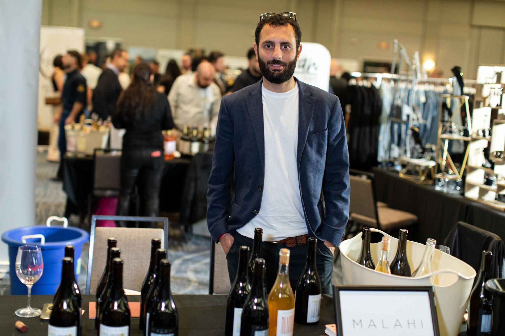 A man stands surrounded by bottles of wine at a wine festival.